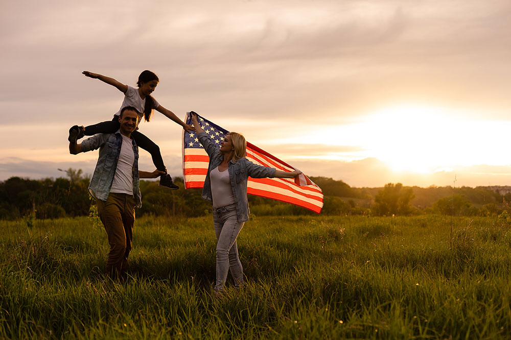 family waving American flag in a field
